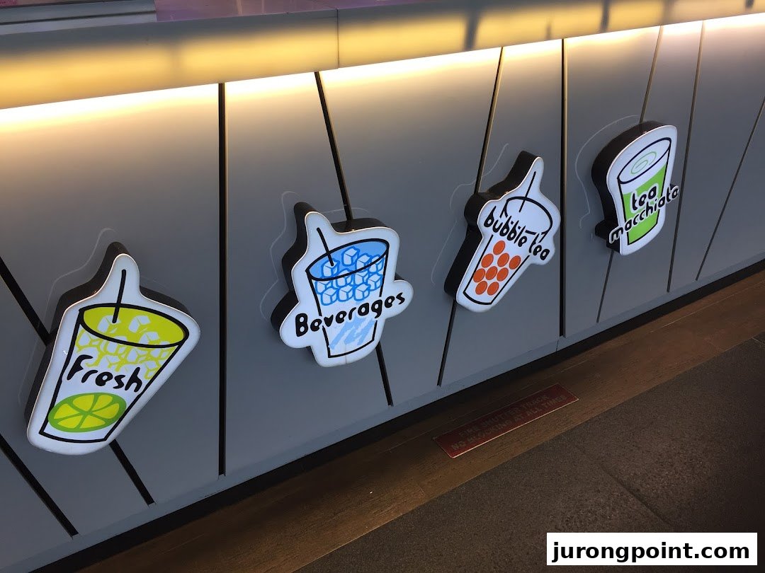 Decorative signs for fresh drinks, beverages, bubble tea, and tea macchiato on a shop counter.