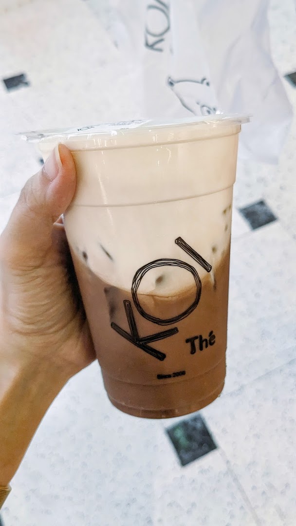 A hand holds a refreshing KOI Thé bubble tea with a creamy top layer.