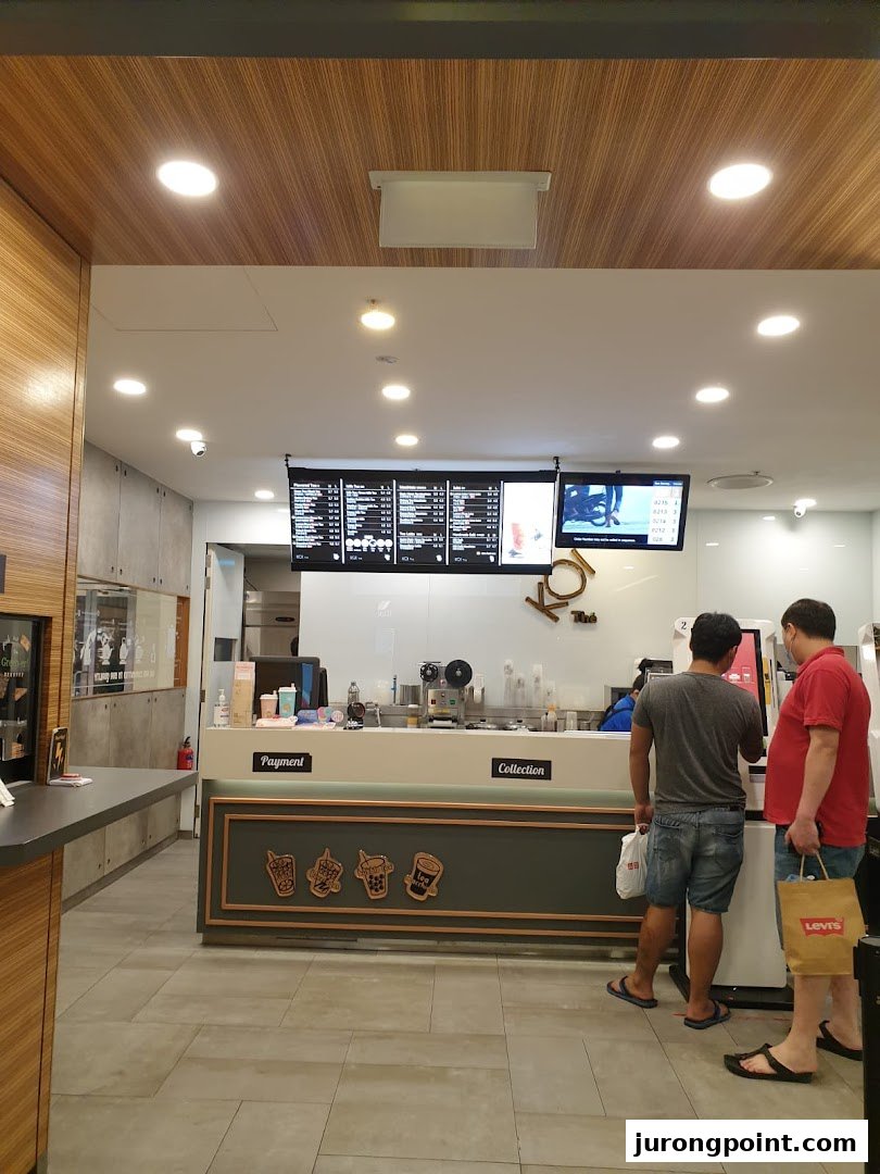 Interior view of KOI Thé with customers at the counter and digital menu boards displaying beverage options.