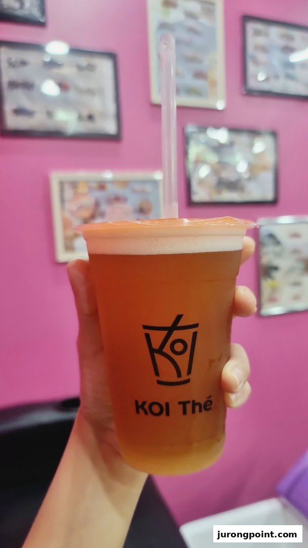 A hand holds a refreshing KOI Thé drink with a pink background and framed pictures.