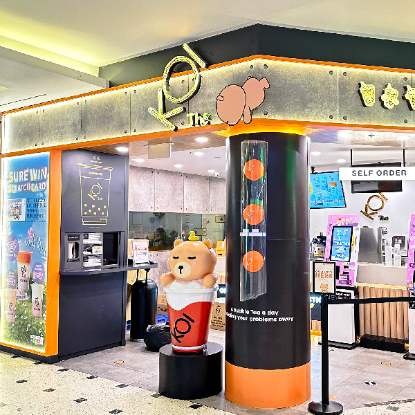 The vibrant storefront of KOI Thé, featuring its logo, a large bear mascot, and self-order stations.