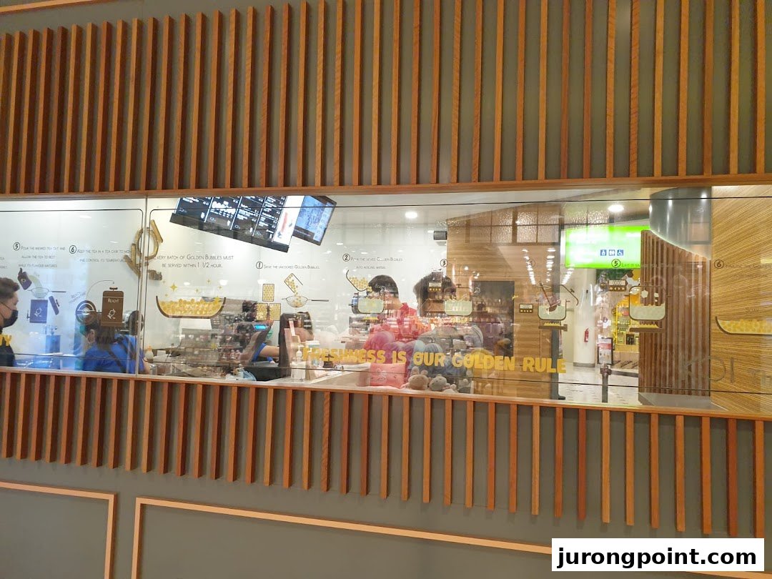 An interior view of KOI Thé, showcasing the preparation area and staff through a large glass window.