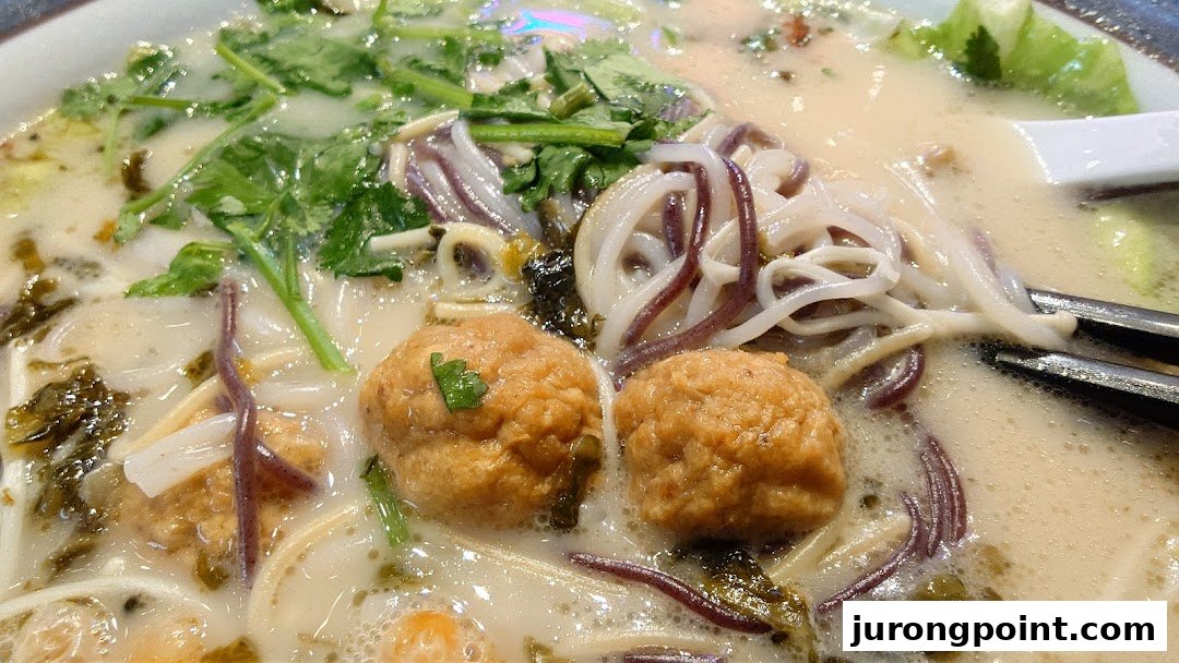 A close-up of a creamy noodle soup with meatballs, various noodles, and fresh greens.