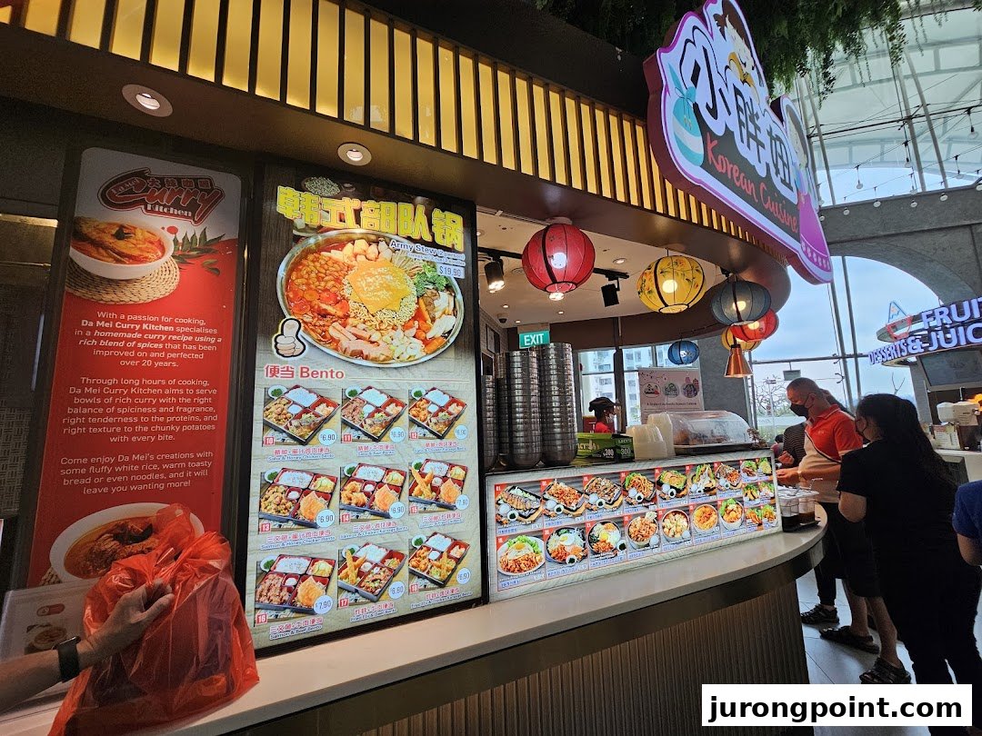 A vibrant food stall in a food hall, showcasing Korean and Curry cuisine displays with customers ordering.