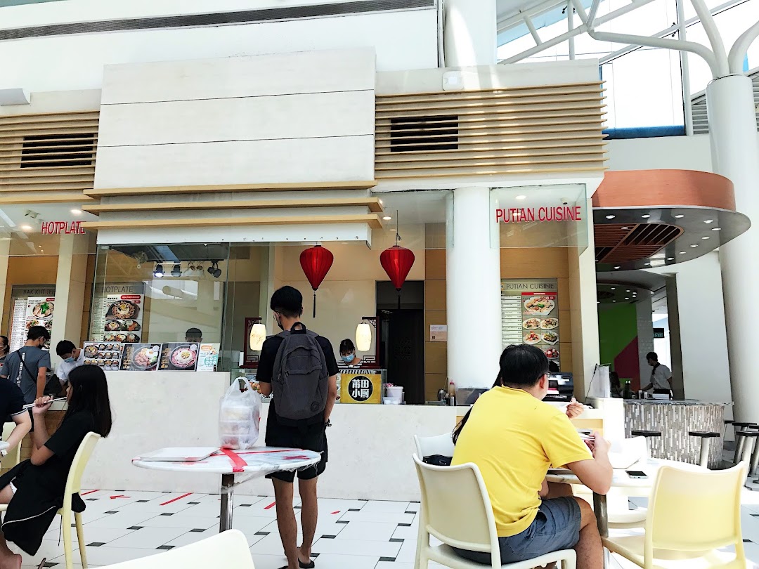 Diners enjoying meals at various food stalls within a bright, spacious food hall.