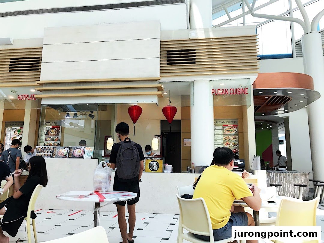 Diners enjoying meals at various food stalls within a bright, spacious food hall.