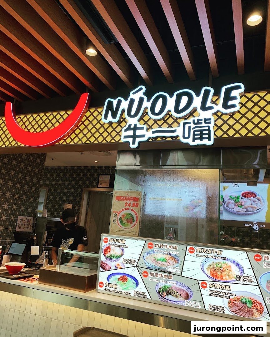 A vibrant noodle stall counter featuring a detailed menu board and a staff member.