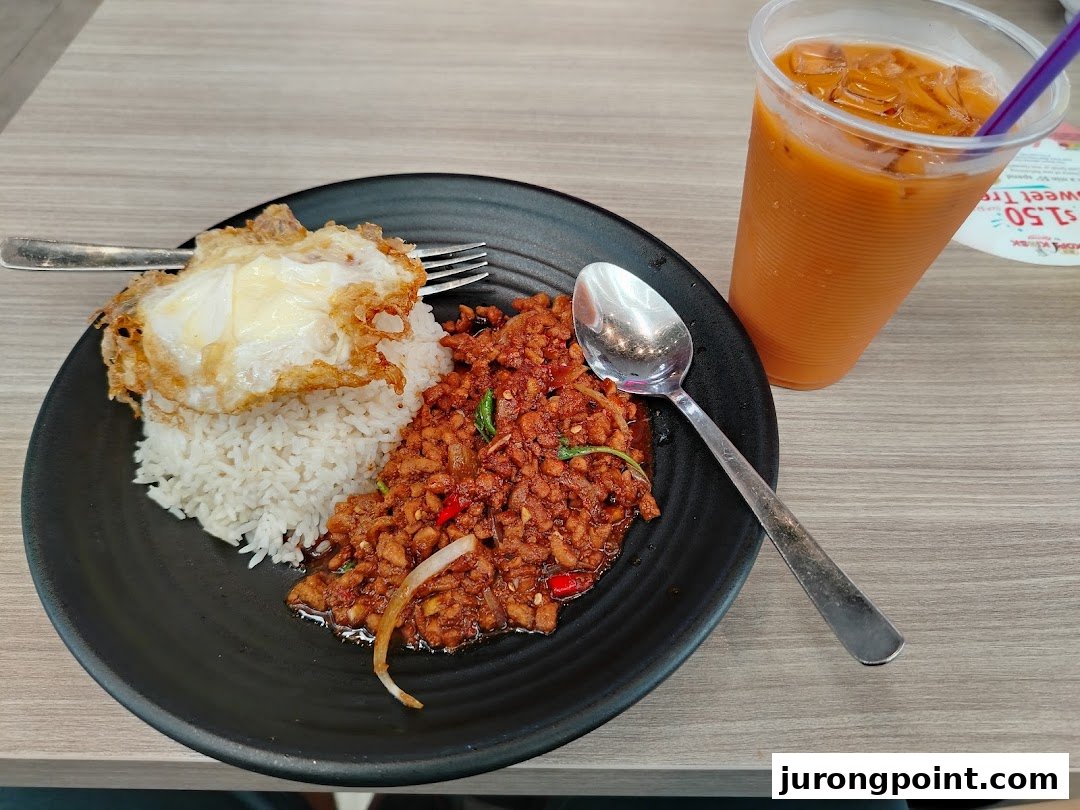 A plate of spicy minced meat with rice and a fried egg, served with an iced Thai milk tea.