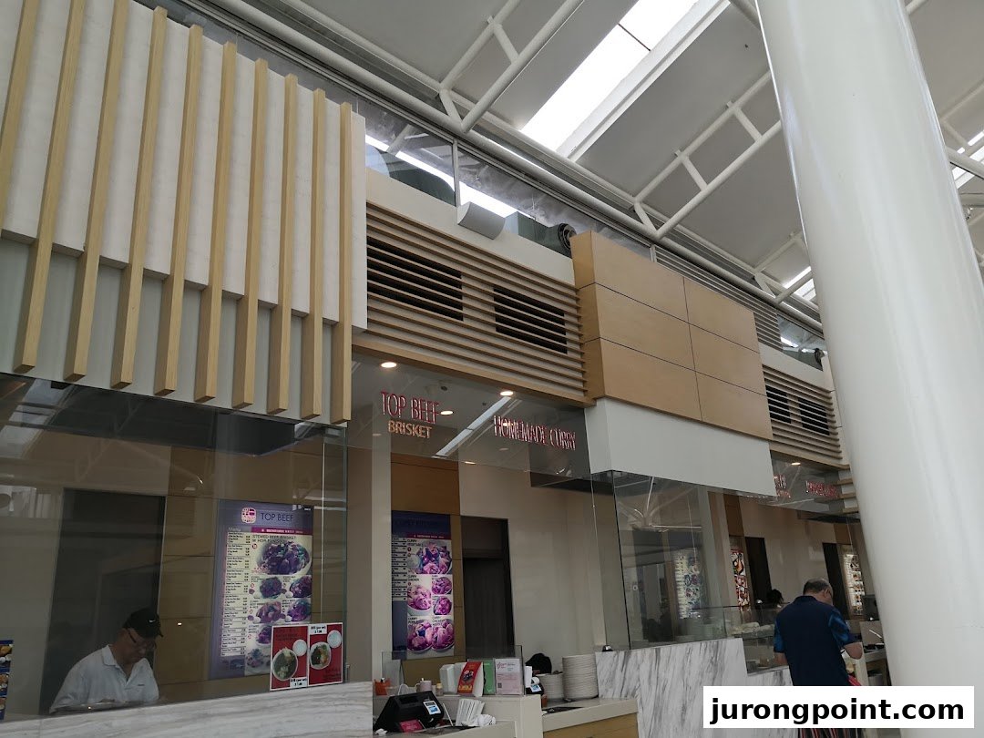 A bright interior view of a food stall within Kopitiam Food Hall, featuring menu displays and service counter.