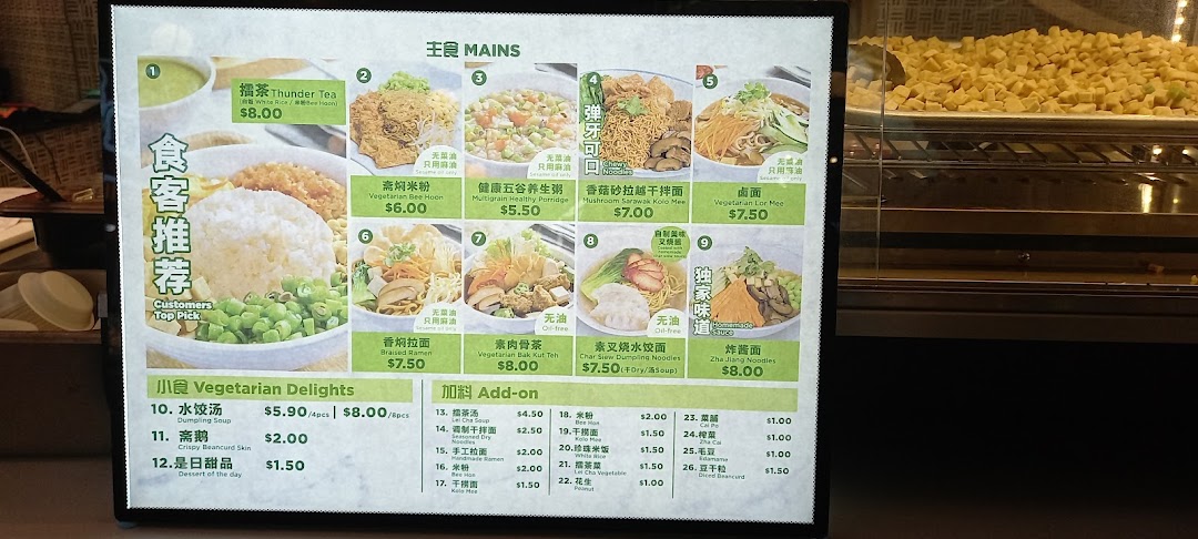 A brightly lit menu board displaying various vegetarian mains, delights, and add-ons with prices.