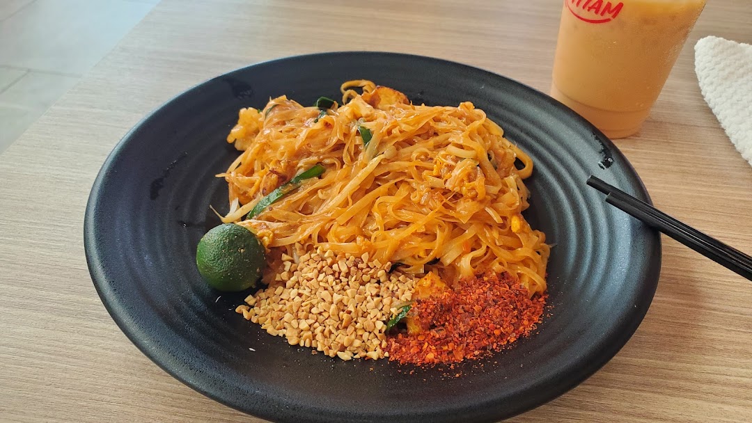 A vibrant plate of Pad Thai with lime, peanuts, and chili flakes, alongside a refreshing drink.