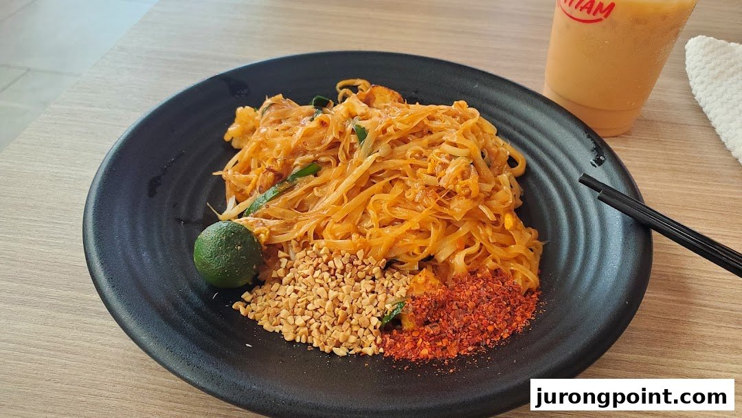 A vibrant plate of Pad Thai with lime, peanuts, and chili flakes, alongside a refreshing drink.
