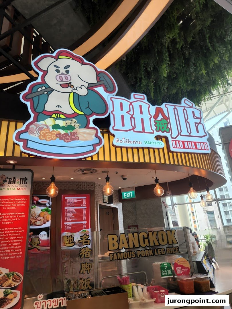 The vibrant storefront of Ba Jie Kao Kha Moo, a Thai pork leg rice stall, within a food hall.