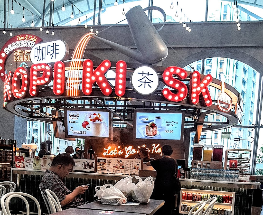 A vibrant Kopikiosk stall in a food hall, featuring neon signs, digital menus, and customers.