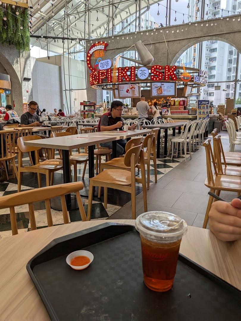 A vibrant interior view of Kopitiam Food Hall, featuring diners, tables, and a refreshing drink in the foreground.