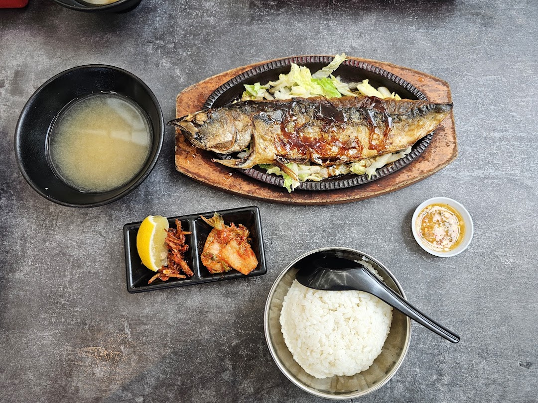 A delicious grilled fish meal with rice, soup, and side dishes on a dark table.