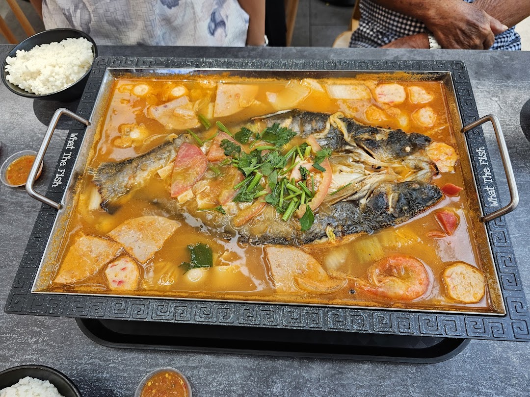 A large, flavorful hotpot with a whole fish, vegetables, and seafood, served with rice.