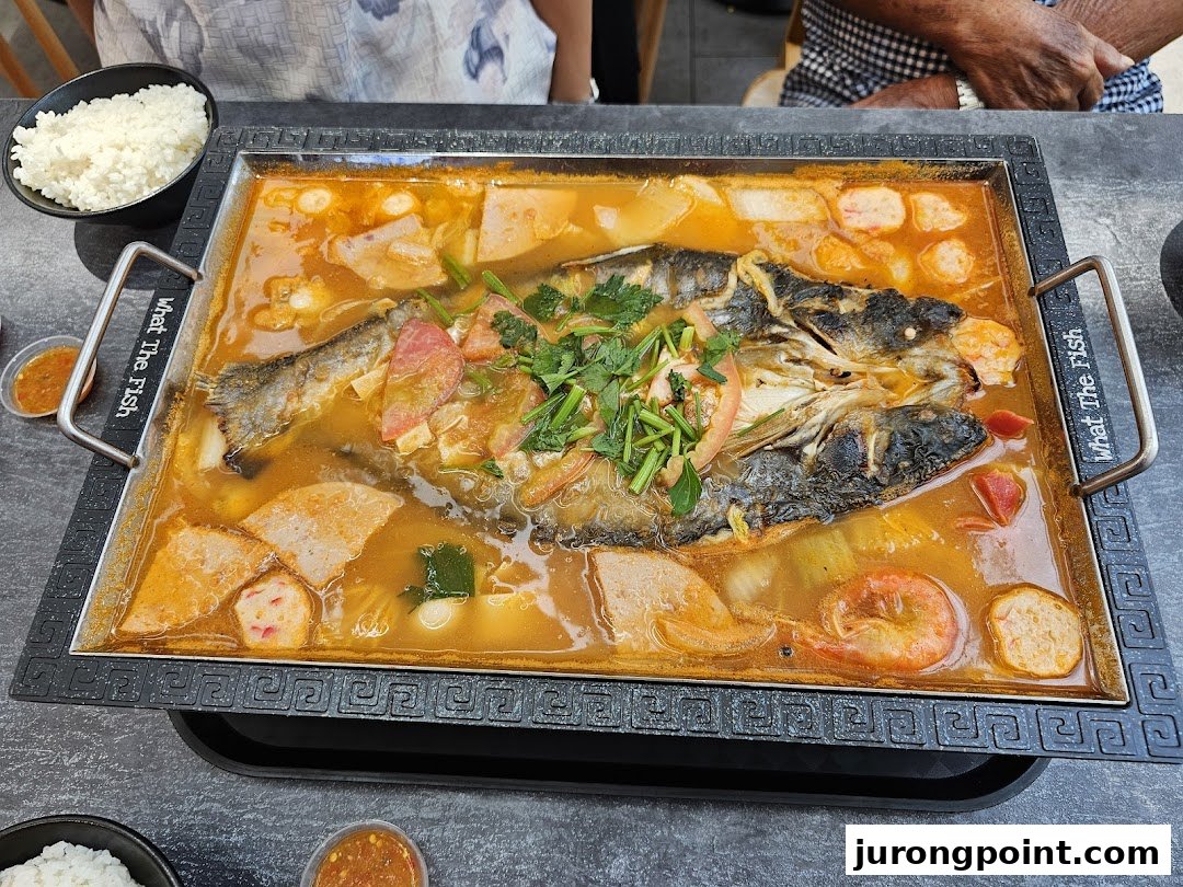 A large, flavorful hotpot with a whole fish, vegetables, and seafood, served with rice.
