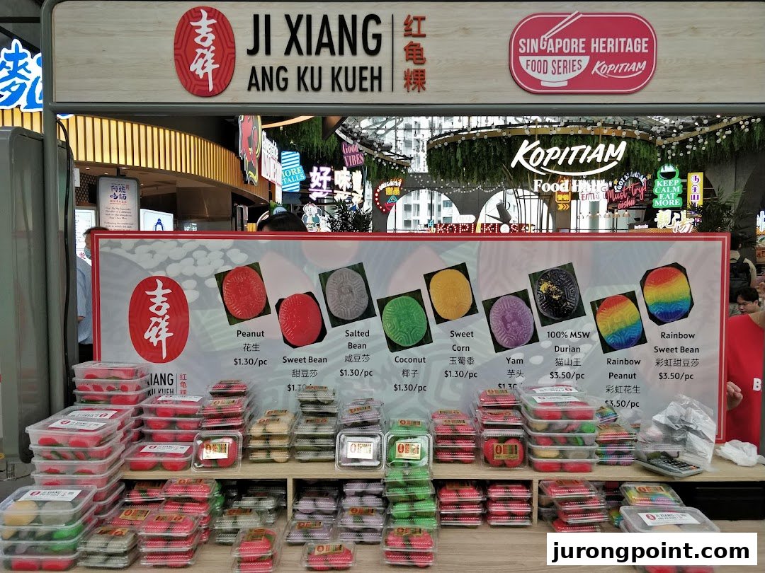 A vibrant display of traditional Ang Ku Kueh pastries with a detailed menu board.