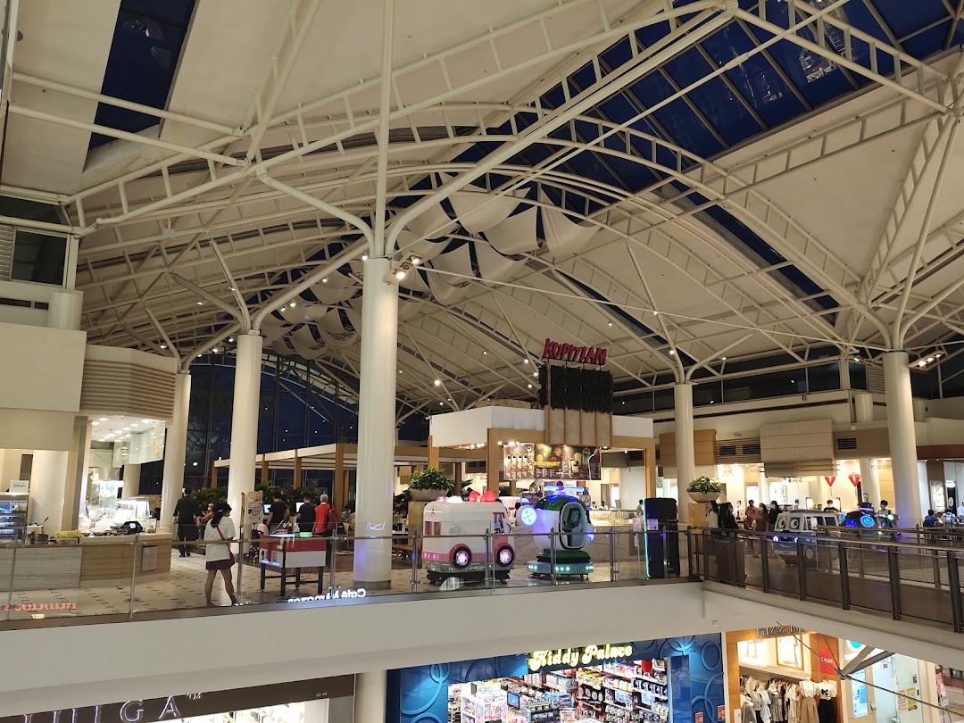 A spacious food hall with various dining options under a high, vaulted ceiling, featuring the Kopitiam sign.