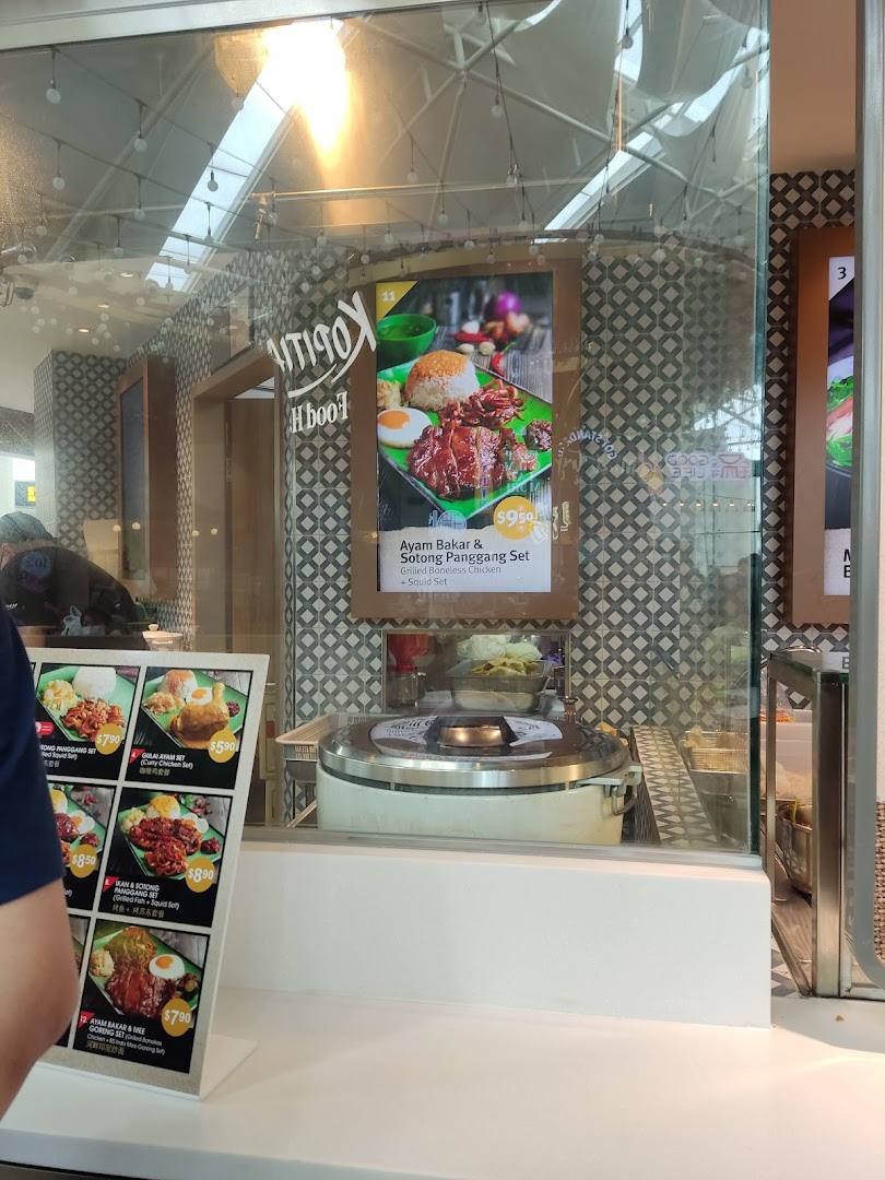 Food counter at Kopitiam Food Hall displaying various Asian set meals with prices and vibrant food photography.