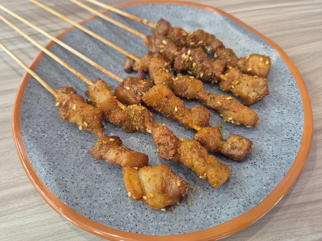 A plate of spiced meat skewers, garnished with sesame seeds and chili flakes.