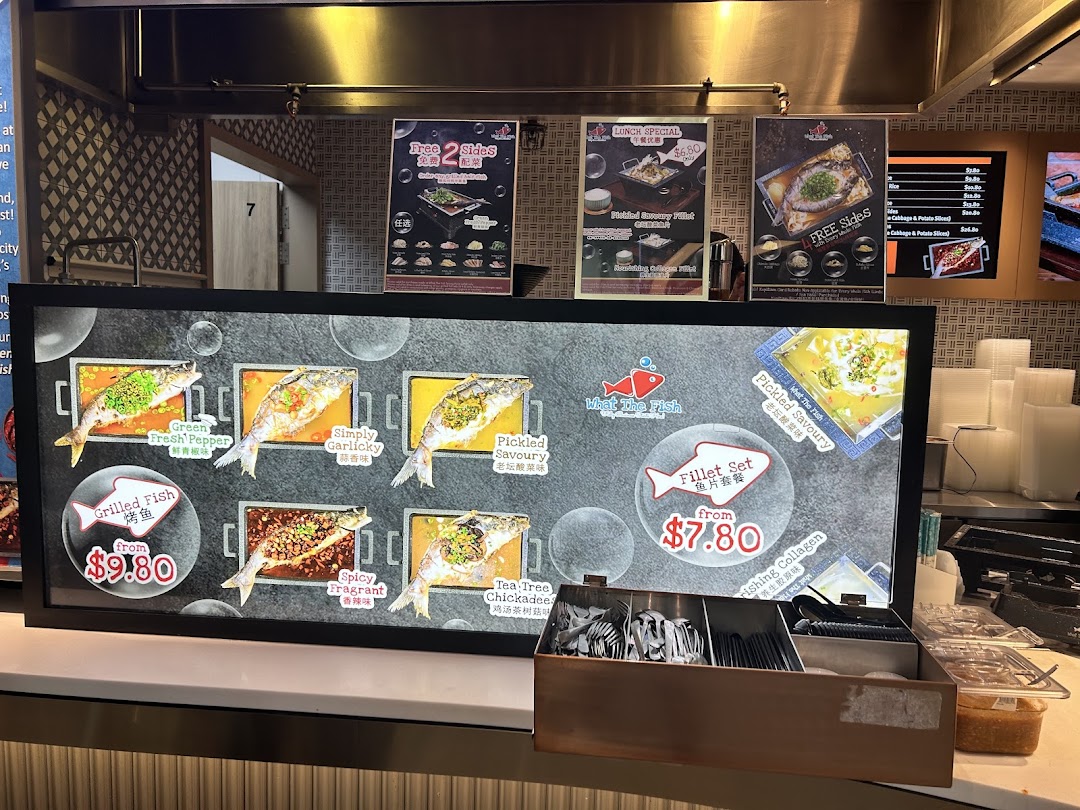 A brightly lit menu board displaying various grilled fish and fillet dishes with prices and promotional posters.