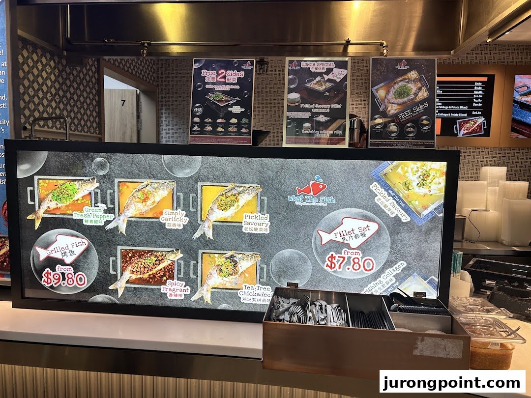 A brightly lit menu board displaying various grilled fish and fillet dishes with prices and promotional posters.
