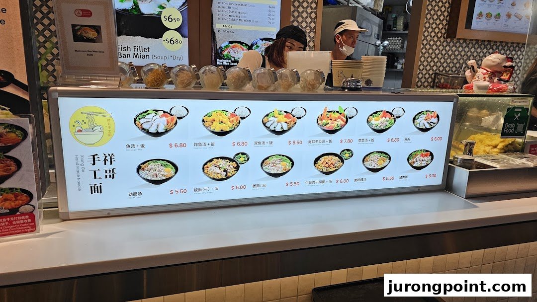 A food stall counter at Kopitiam Food Hall featuring a bright menu display of various noodle and rice dishes.