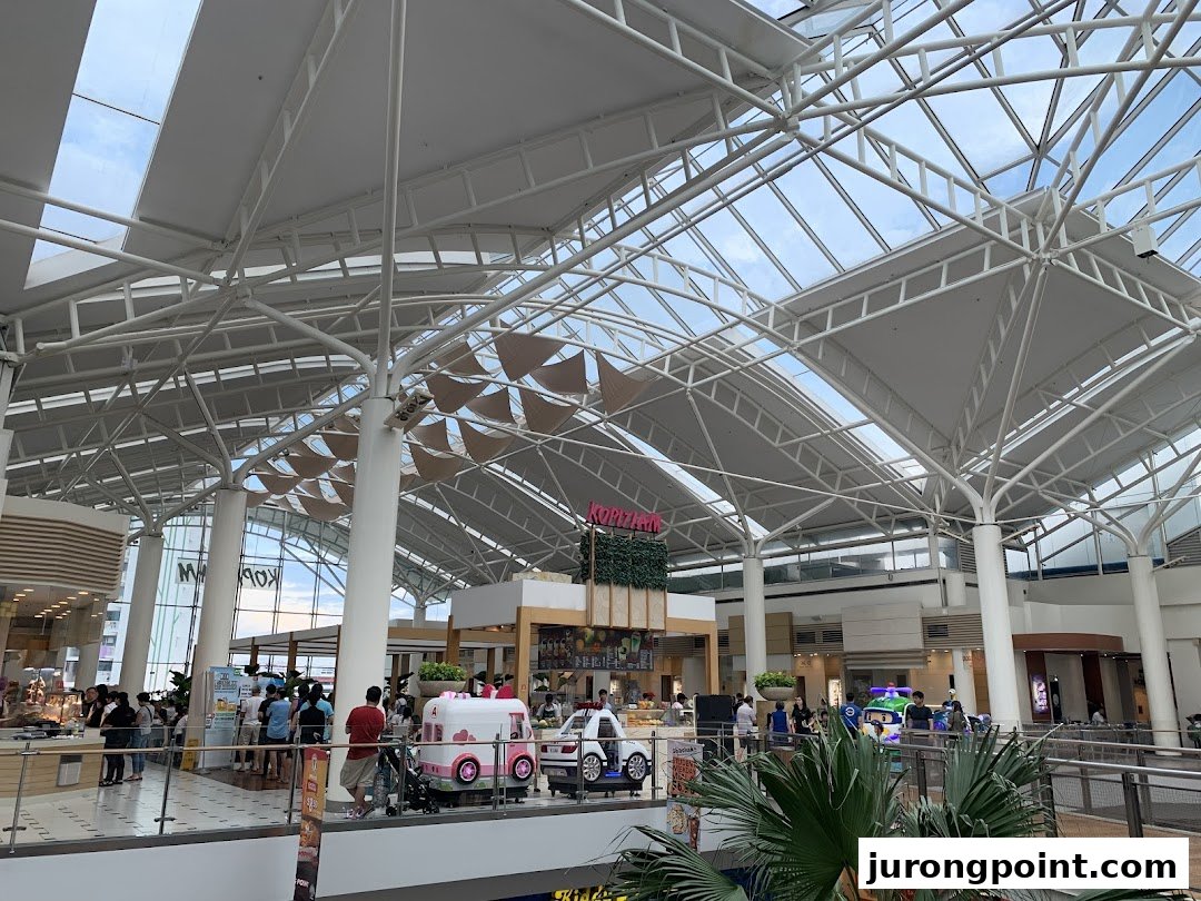 A spacious food hall interior with high ceilings, various food stalls, and people dining.