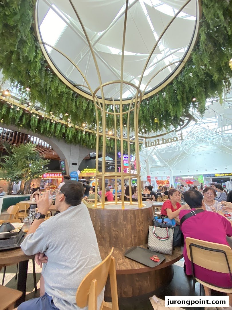 A vibrant interior view of Kopitiam Food Hall, featuring diners and a large decorative centerpiece.