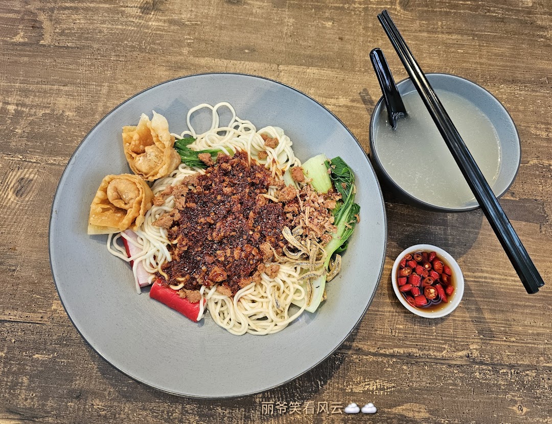 A delicious plate of dry noodles with minced meat, vegetables, fried wontons, and a side of soup and chili.