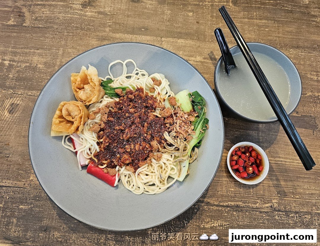 A delicious plate of dry noodles with minced meat, vegetables, fried wontons, and a side of soup and chili.