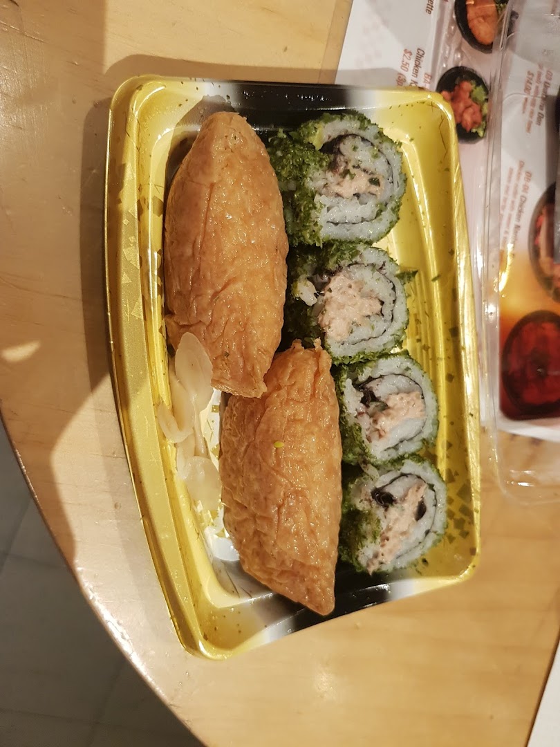 A take-out container with inari sushi and maki rolls, with a partial menu visible in the background.