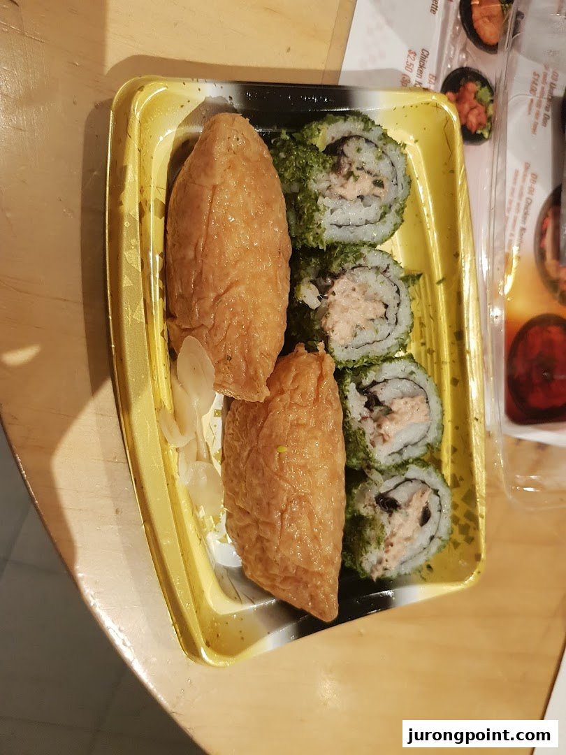 A take-out container with inari sushi and maki rolls, with a partial menu visible in the background.