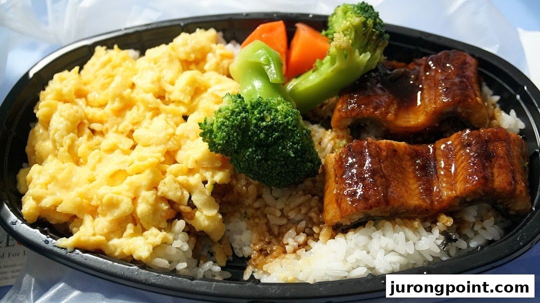 A bento box featuring glazed eel, fluffy scrambled eggs, rice, and steamed vegetables.