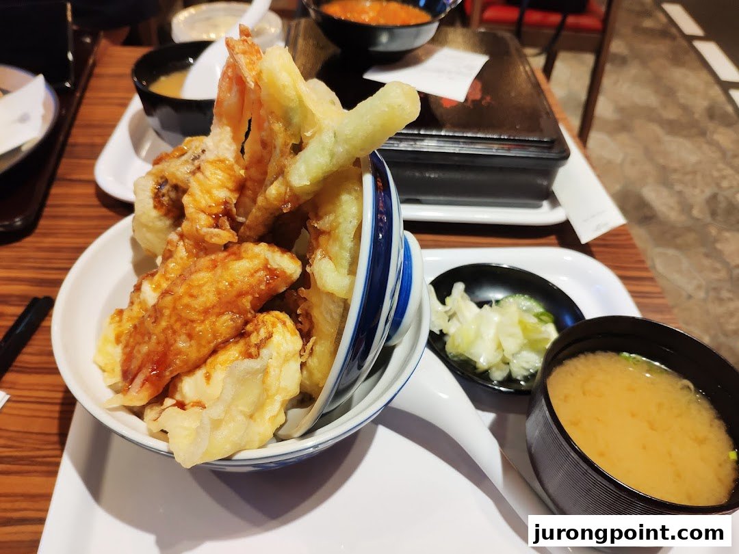 A close-up of a delicious Japanese tempura bowl served with miso soup and pickles.