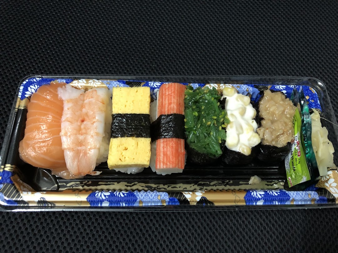 A vibrant assortment of fresh sushi pieces, including salmon, shrimp, and tamago, in a clear takeaway tray.