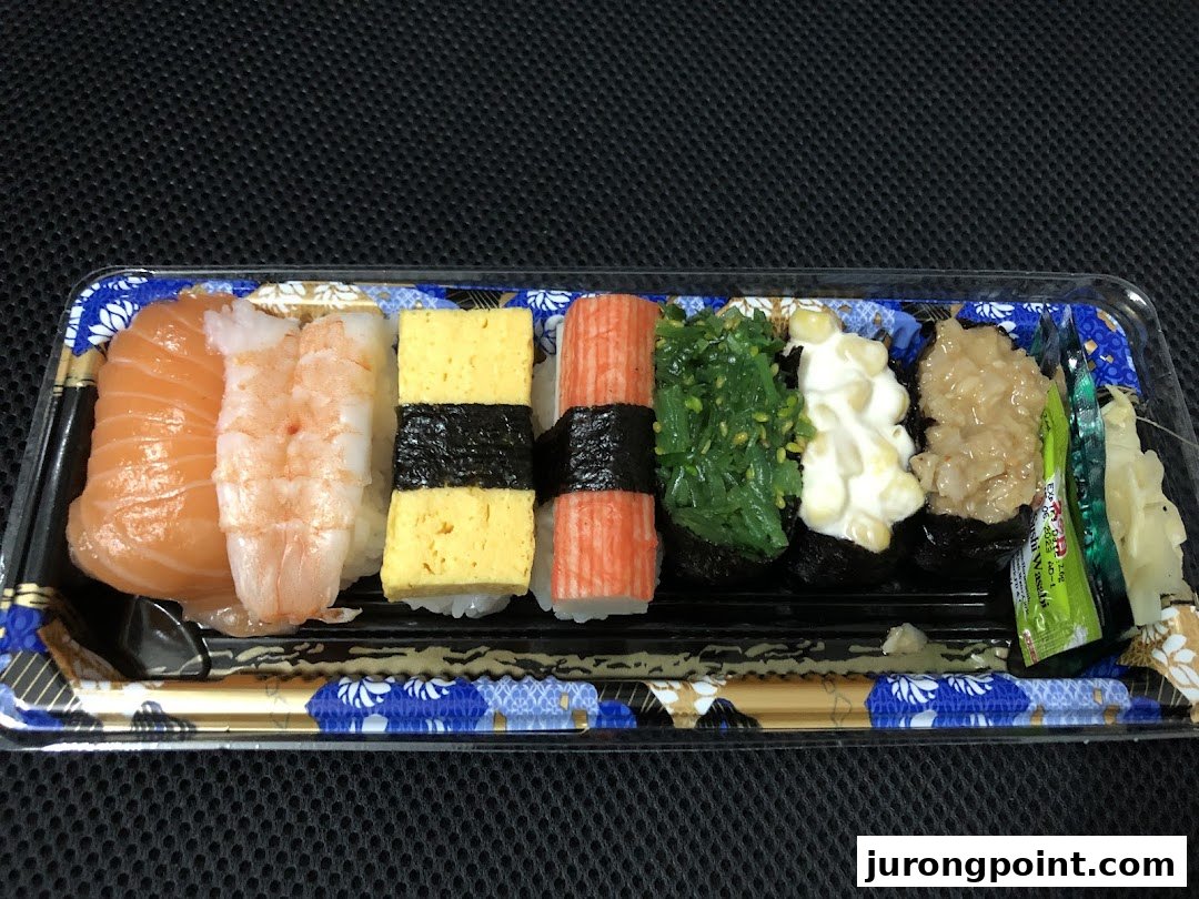 A vibrant assortment of fresh sushi pieces, including salmon, shrimp, and tamago, in a clear takeaway tray.
