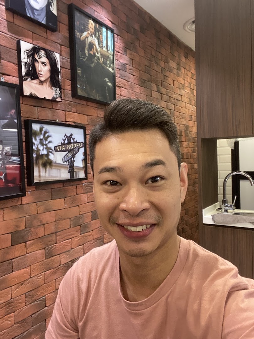 A smiling man in a modern barbershop interior featuring a brick wall, framed art, and a clean sink area.