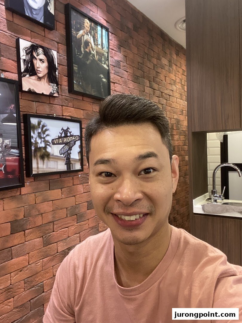 A smiling man in a modern barbershop interior featuring a brick wall, framed art, and a clean sink area.