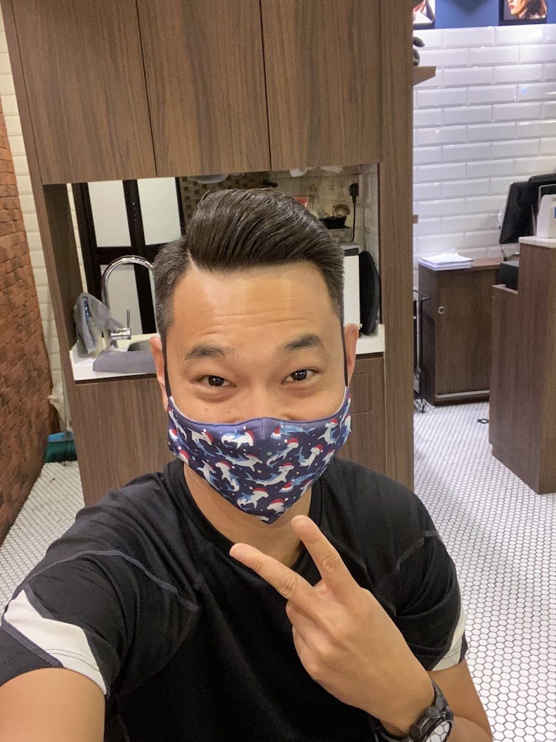 A man with a fresh haircut, wearing a mask, gives a peace sign inside LA Barbershop.