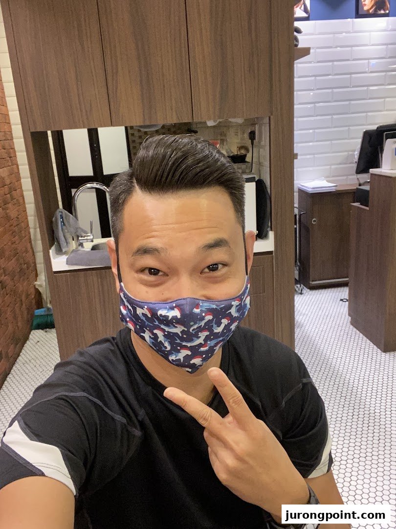 A man with a fresh haircut, wearing a mask, gives a peace sign inside LA Barbershop.