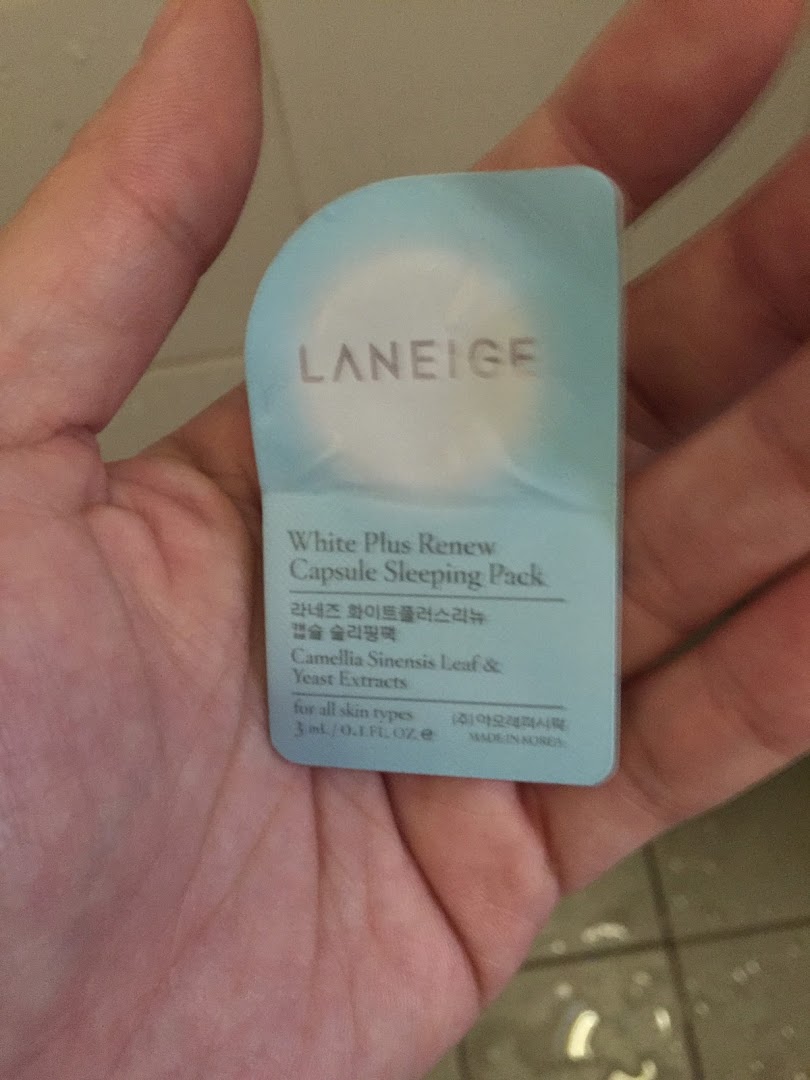A hand holds a sample packet of Laneige White Plus Renew Capsule Sleeping Pack.