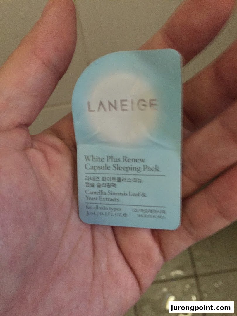 A hand holds a sample packet of Laneige White Plus Renew Capsule Sleeping Pack.