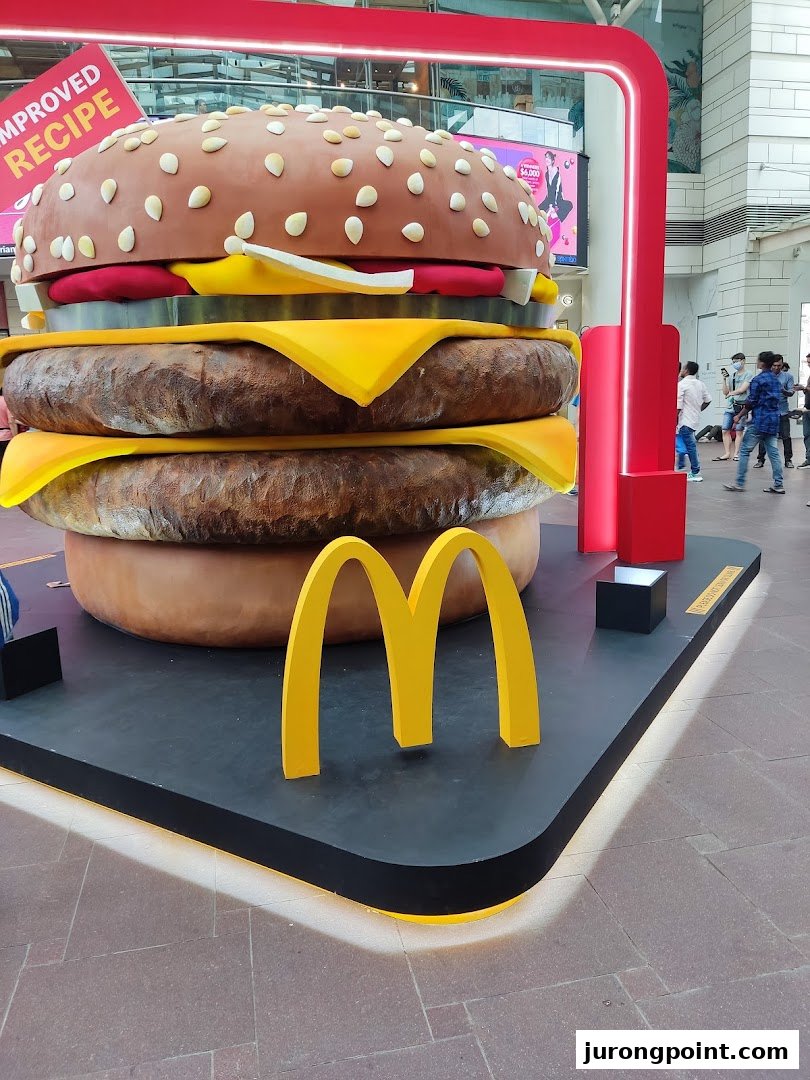 A giant McDonald's burger display with the golden arches, promoting an improved recipe.