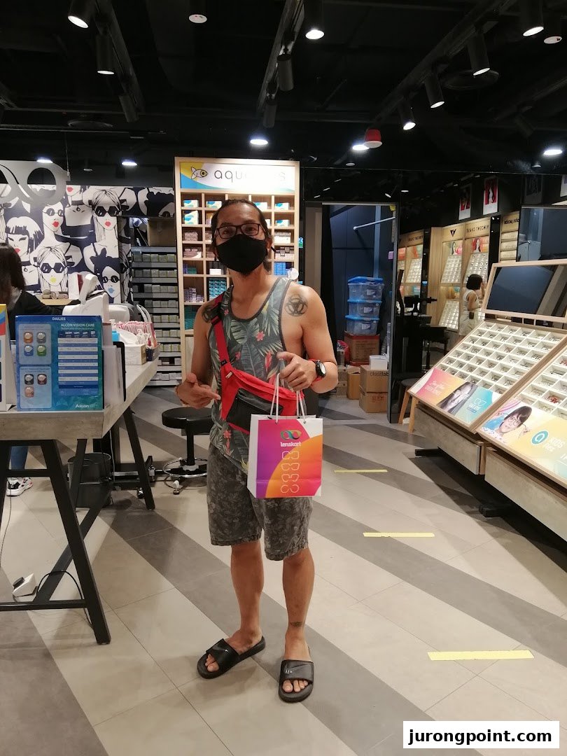 A customer stands inside a Lenskart store, holding a branded shopping bag after a purchase.