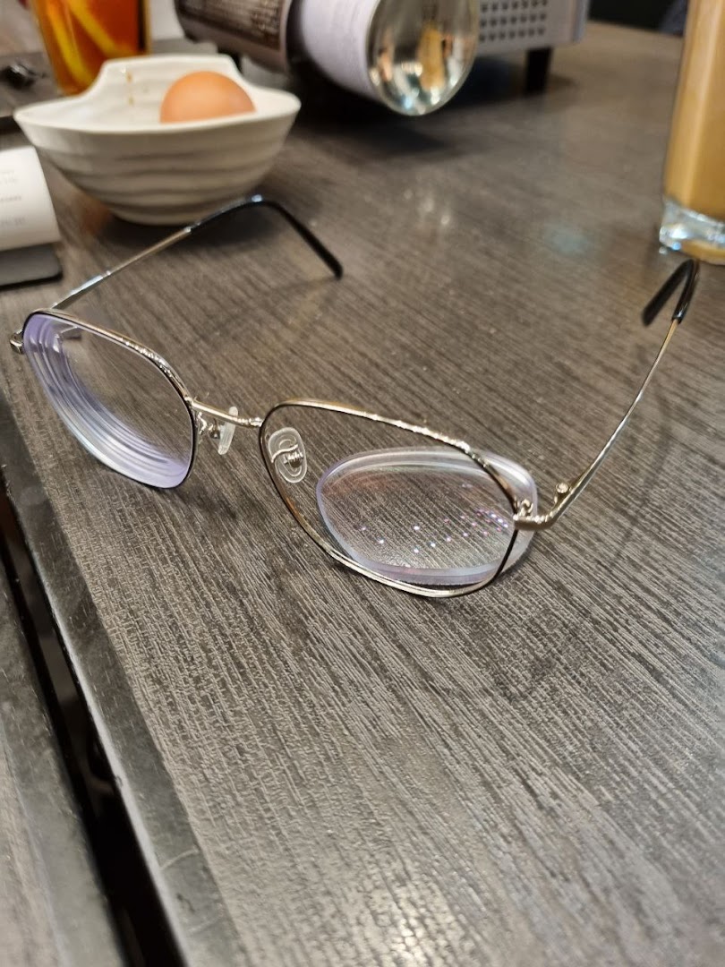 A pair of stylish eyeglasses rests on a wooden table, with a casual dining setting in the background.