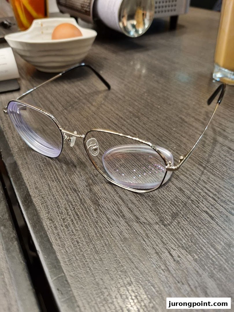 A pair of stylish eyeglasses rests on a wooden table, with a casual dining setting in the background.