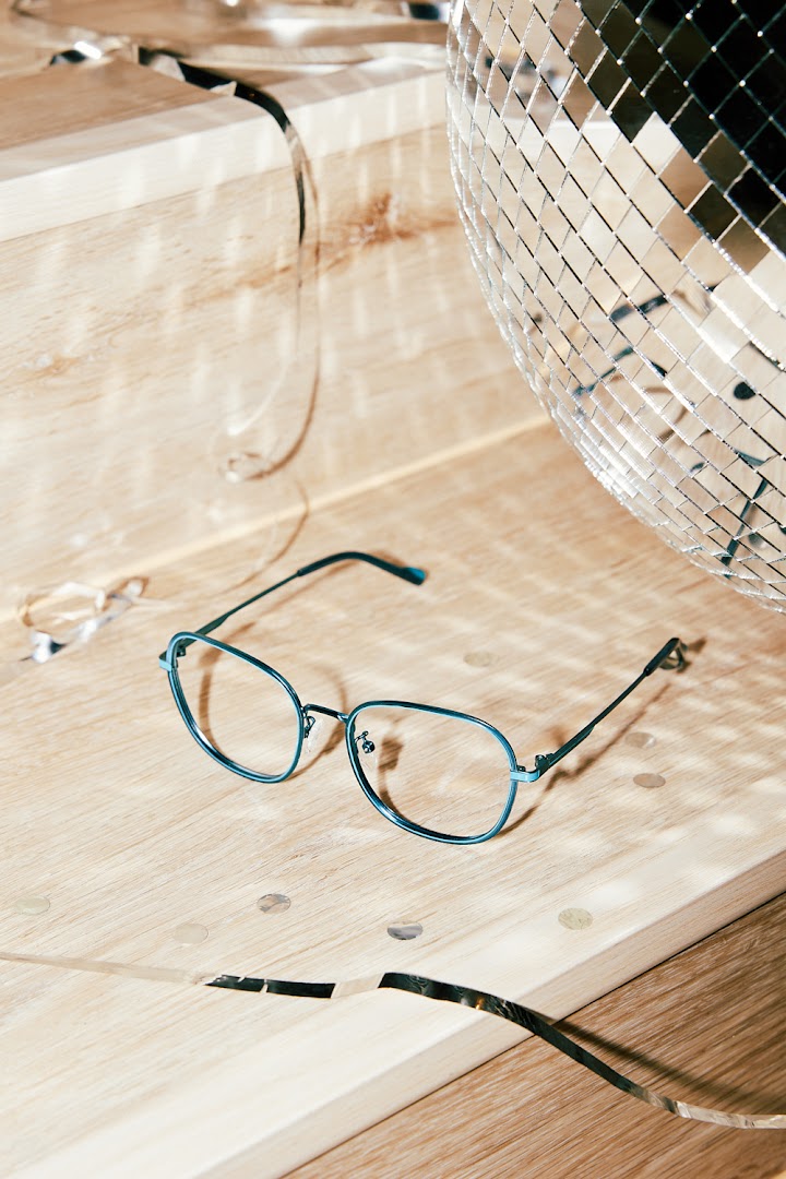 Stylish blue eyeglasses on a wooden surface with a disco ball and confetti.